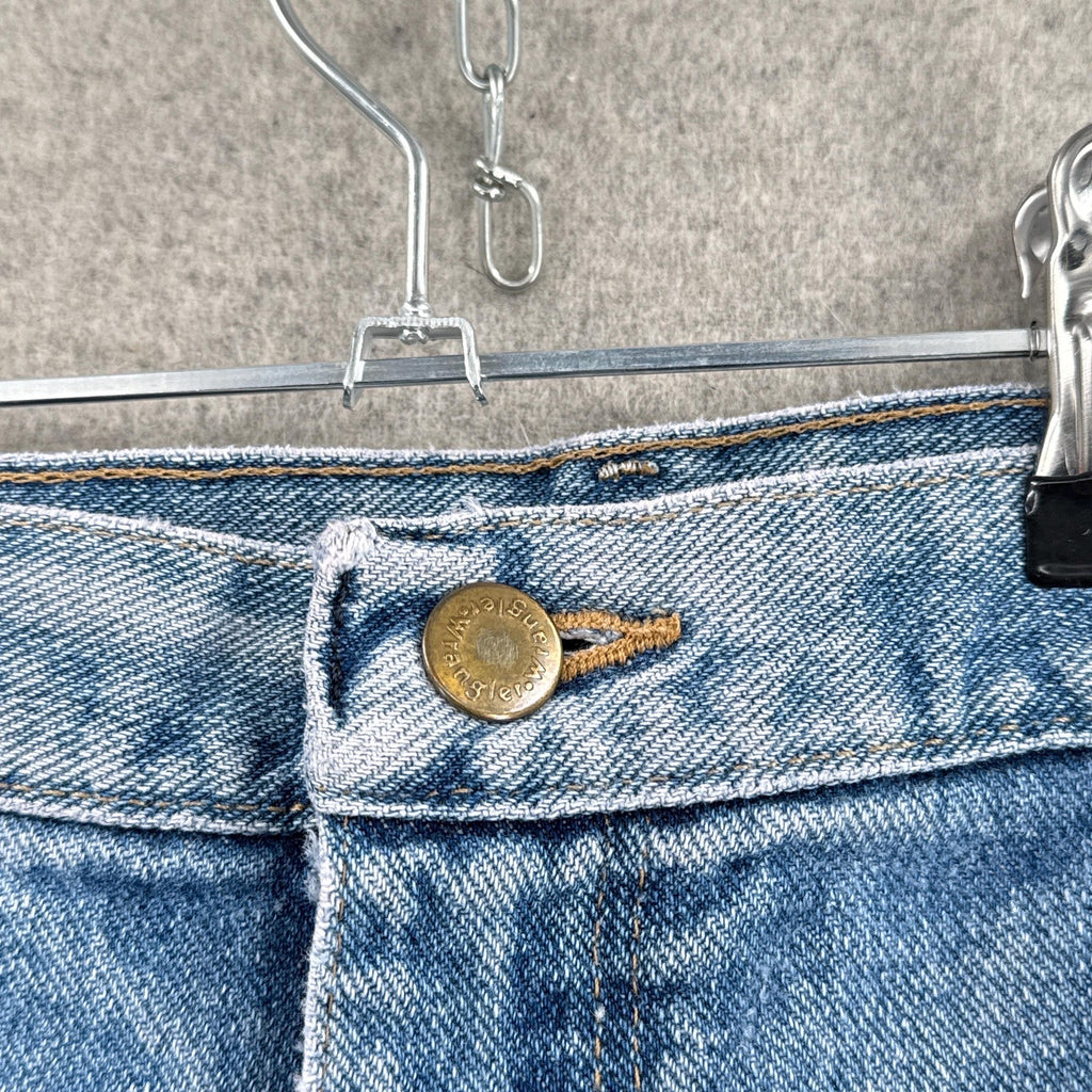 Close-up of blue jeans with a button on a hanger against a neutral background