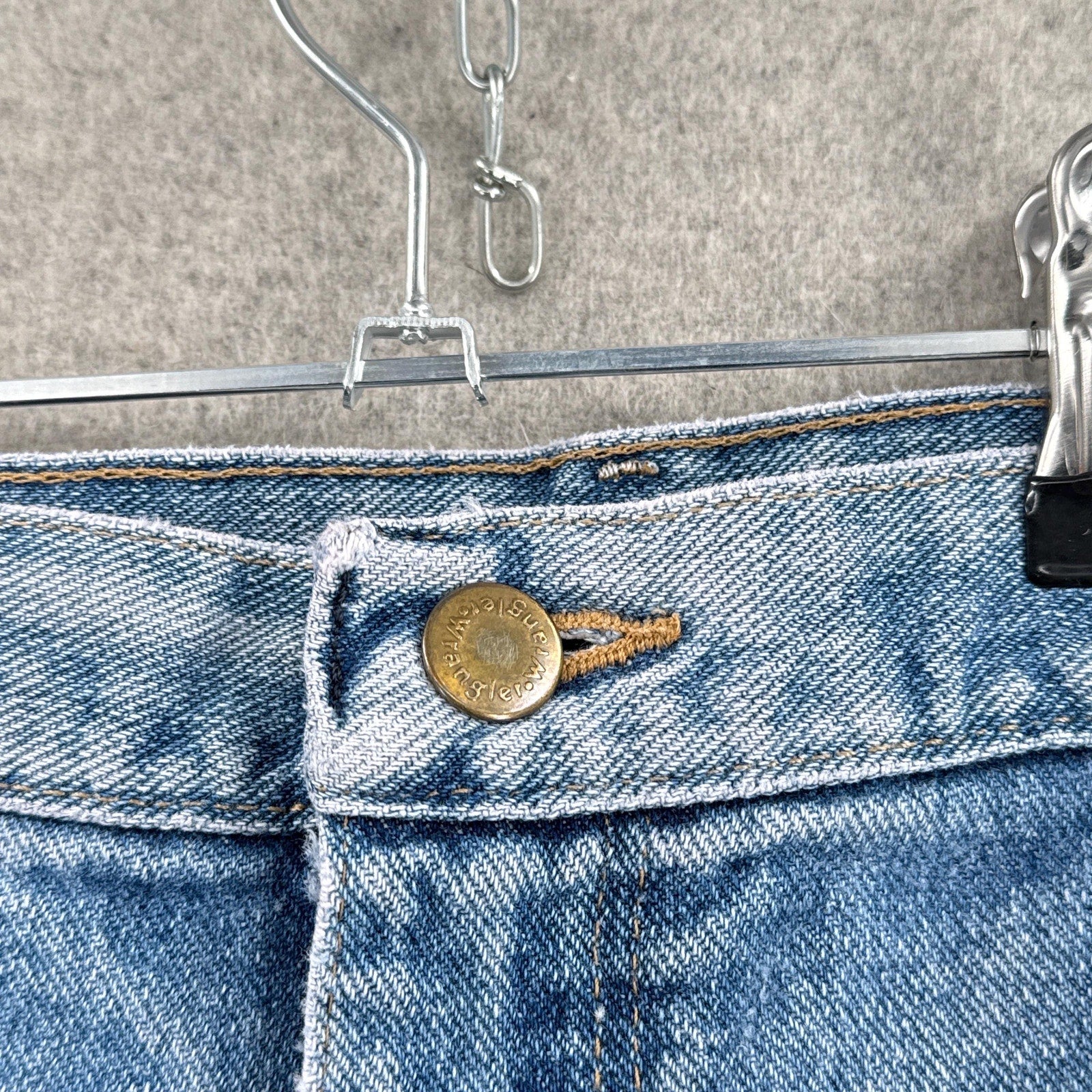 Close-up of blue jeans with a button on a hanger against a neutral background