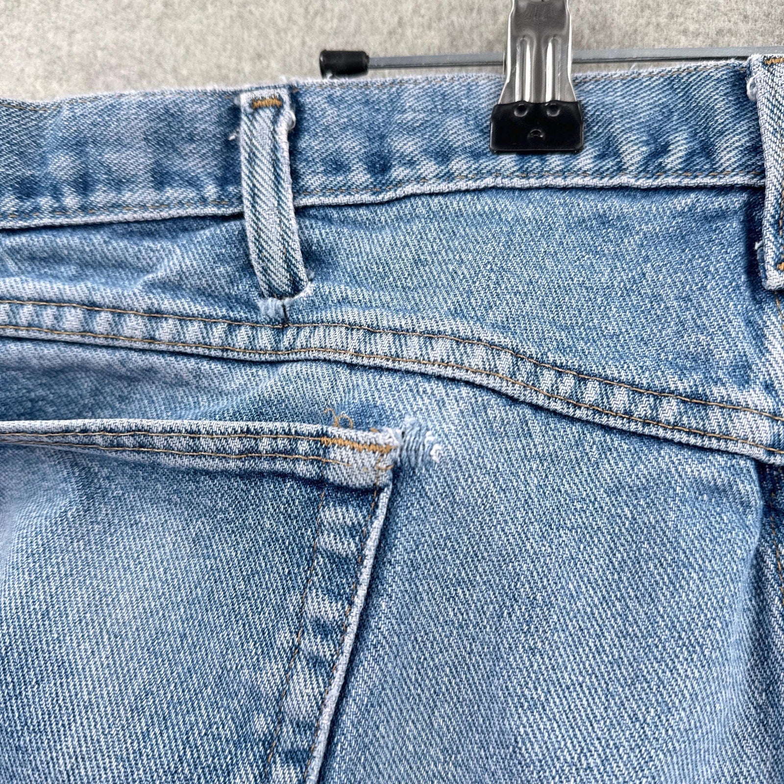 Close-up of blue jeans with a metal clip on a textured surface. rip near pocket