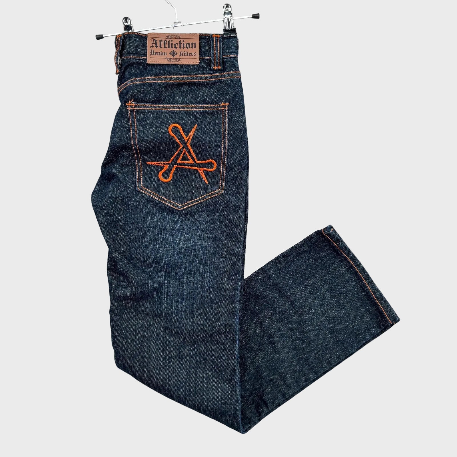 Blue jeans with orange logo on pocket, hanging against a textured white background