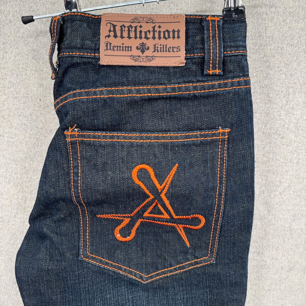 Blue jeans with orange stitching and 'Affliction' brand label on a neutral background