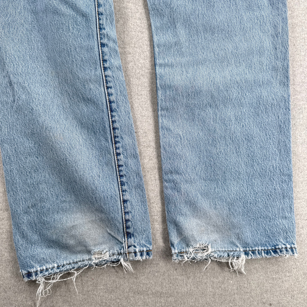 Close-up of light blue jeans with frayed hems on a beige surface