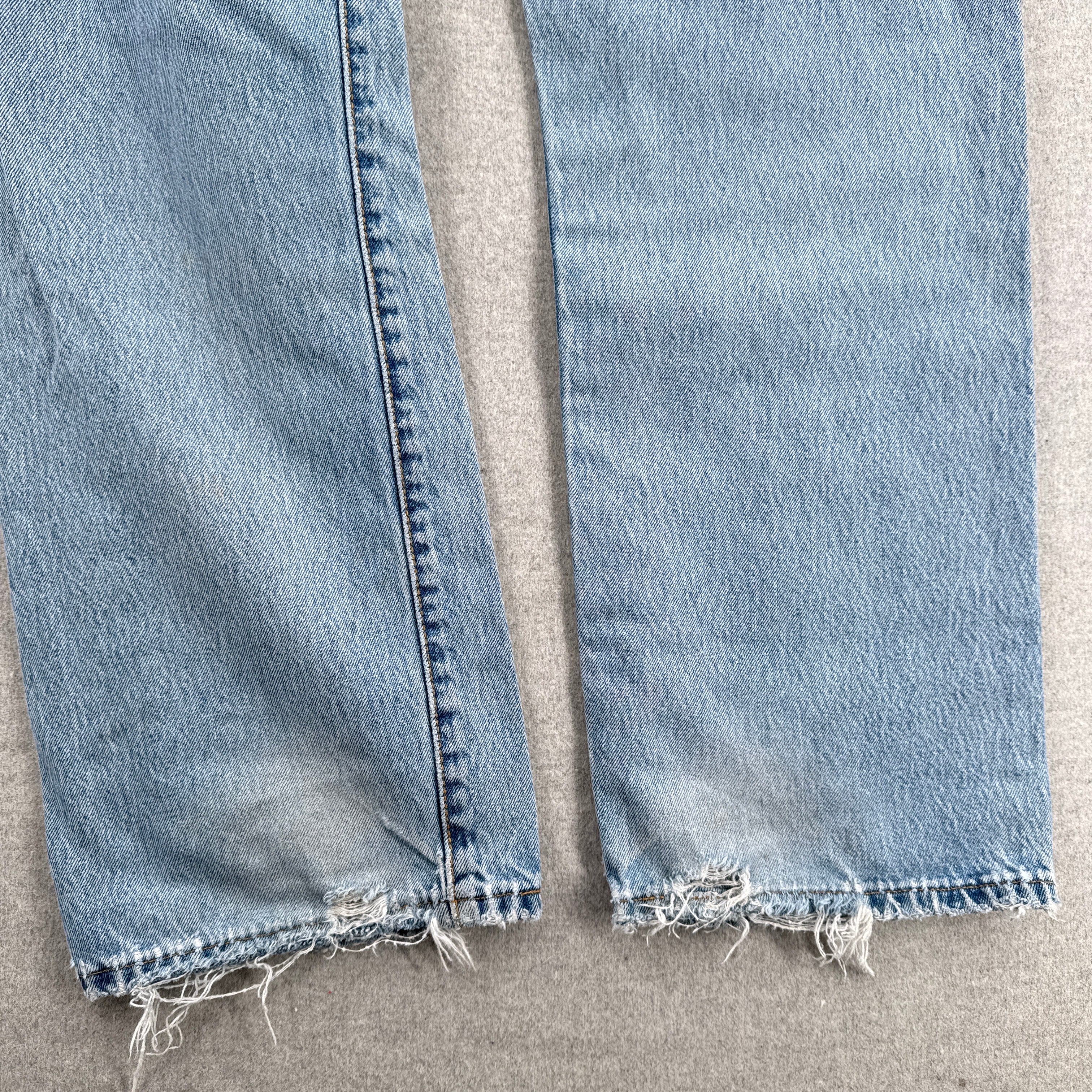 Close-up of light blue jeans with frayed hems on a beige surface