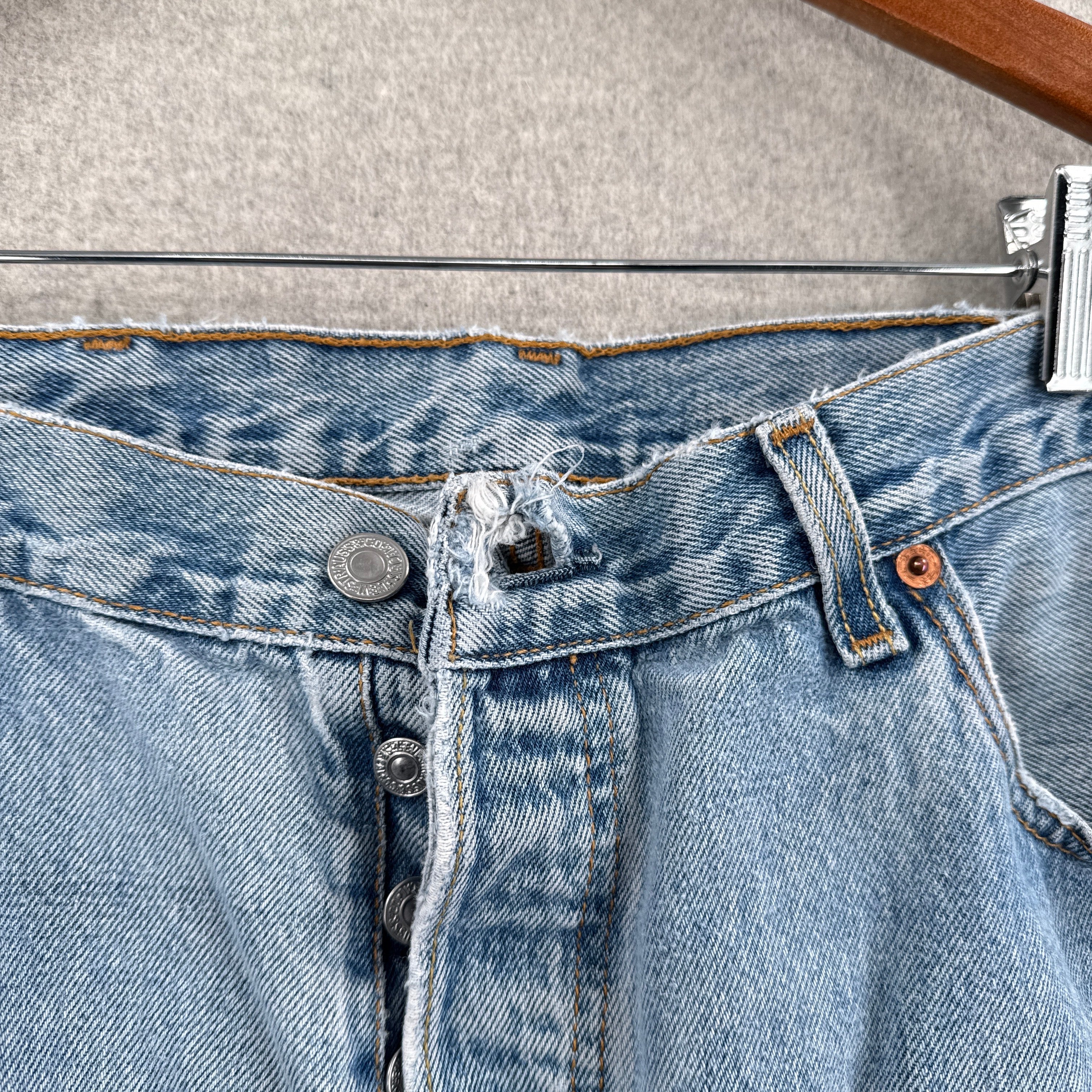 Close-up of a blue denim fabric with stitching details on a gray background. top button loop stretched/hole