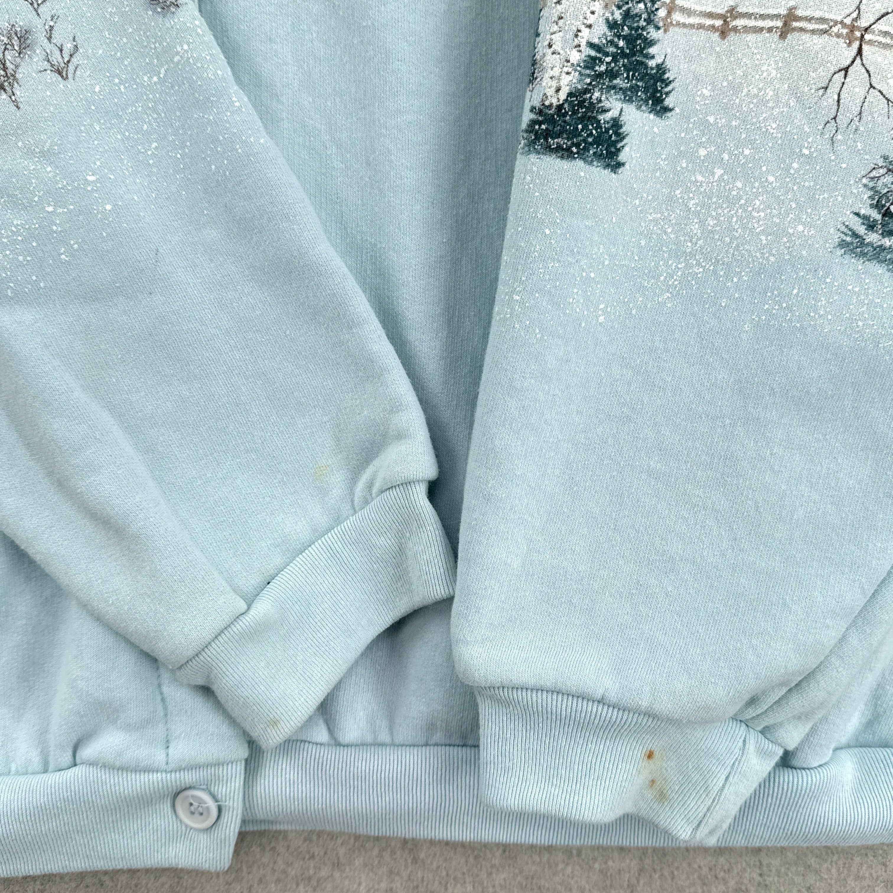 Light blue sweater with snowflakes and trees in the background showing stain spots on bottom of sleeves