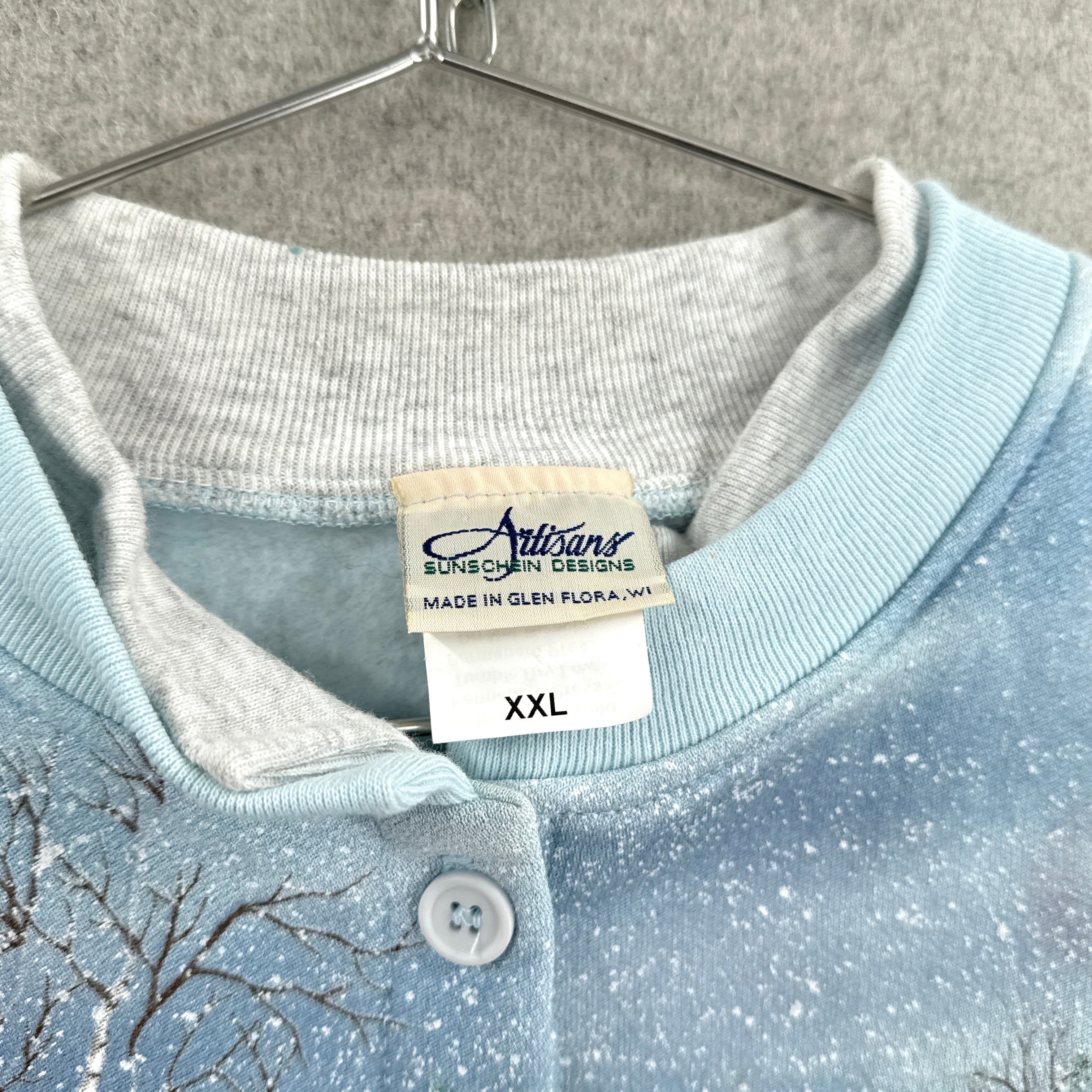 Light blue sweater with a brand label on a gray background. XXL size