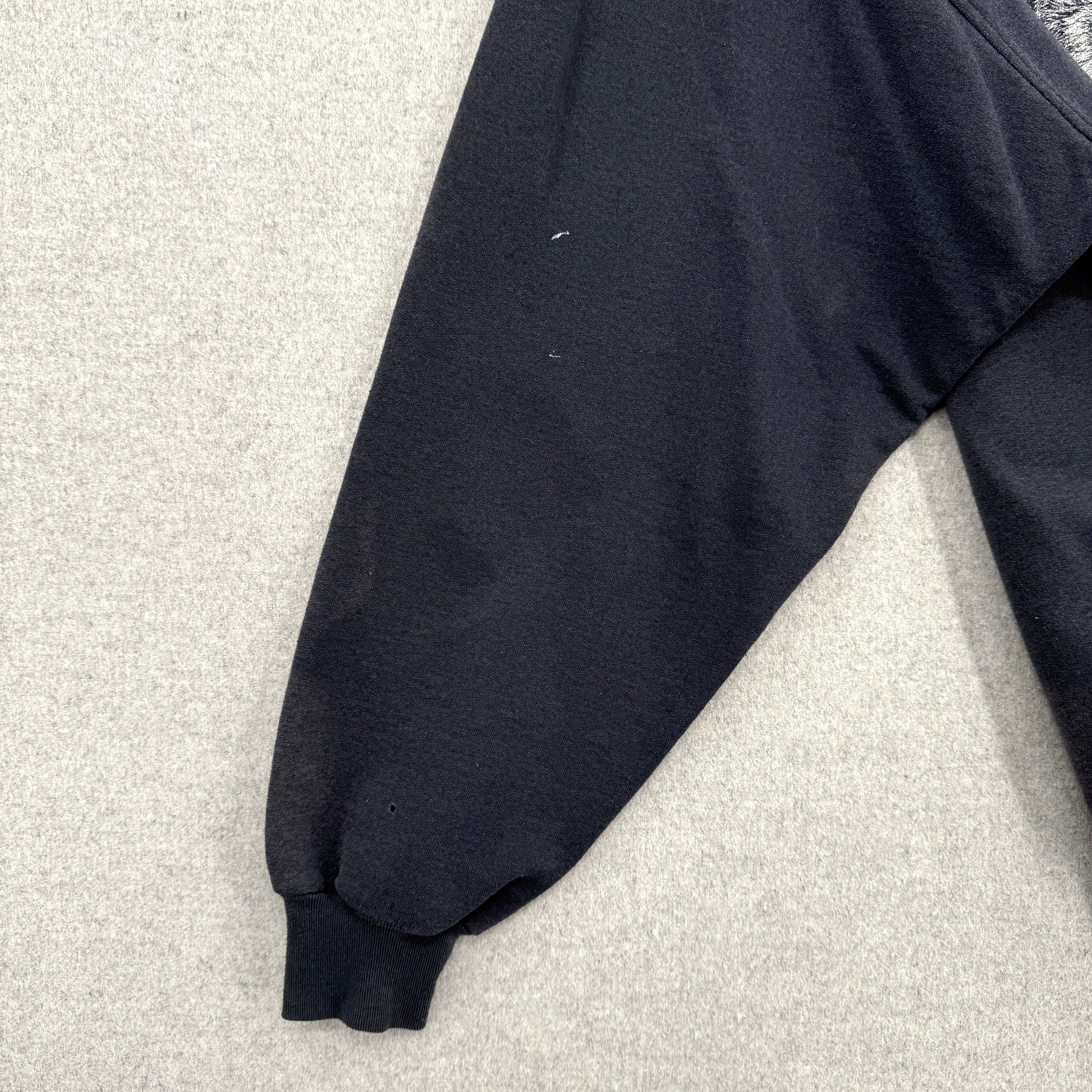 Black sweatshirt sleeve on a light gray surface. Shows some small white stain spots
