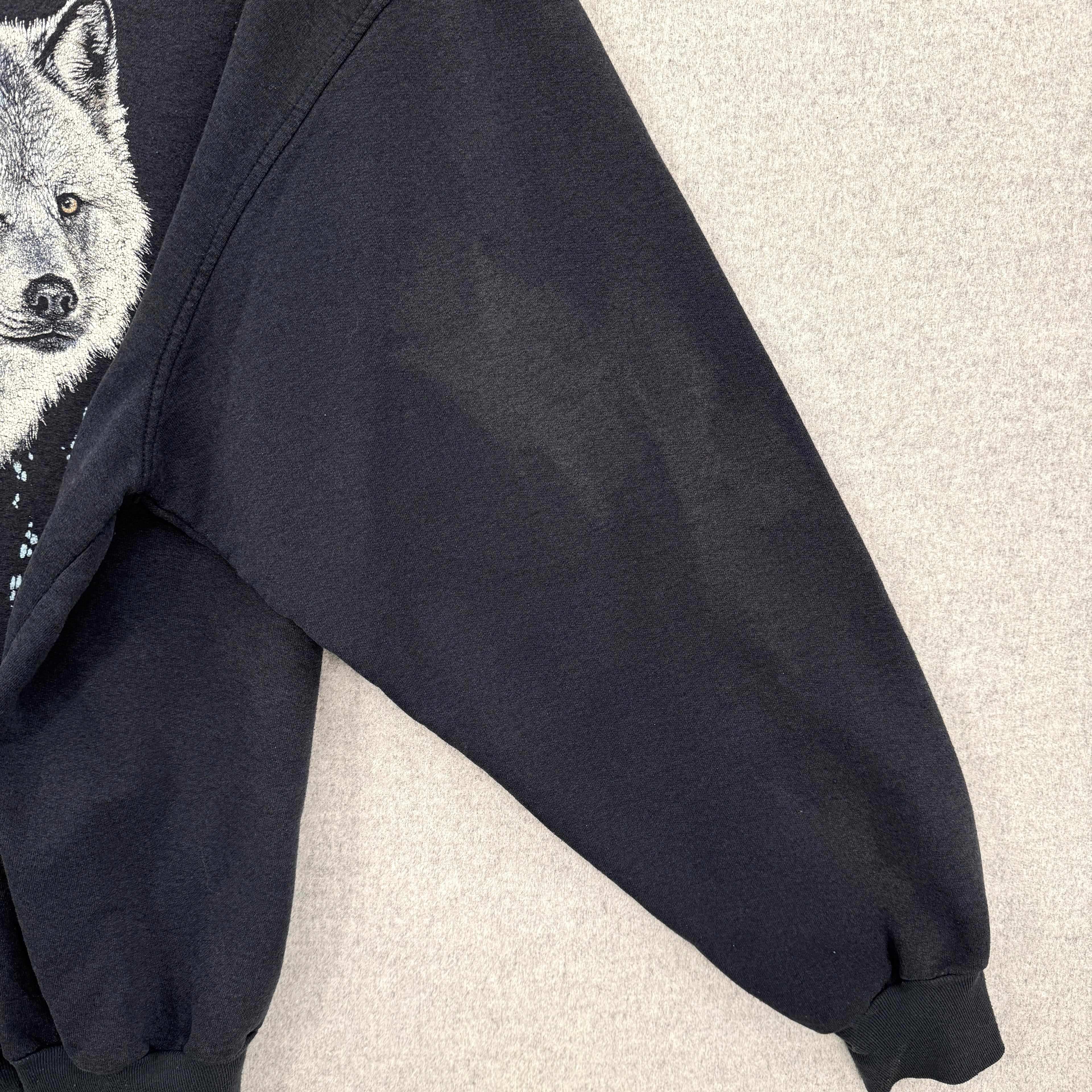 Black hoodie with a wolf graphic on a light gray background. Shows sleeve with lightened discolouration