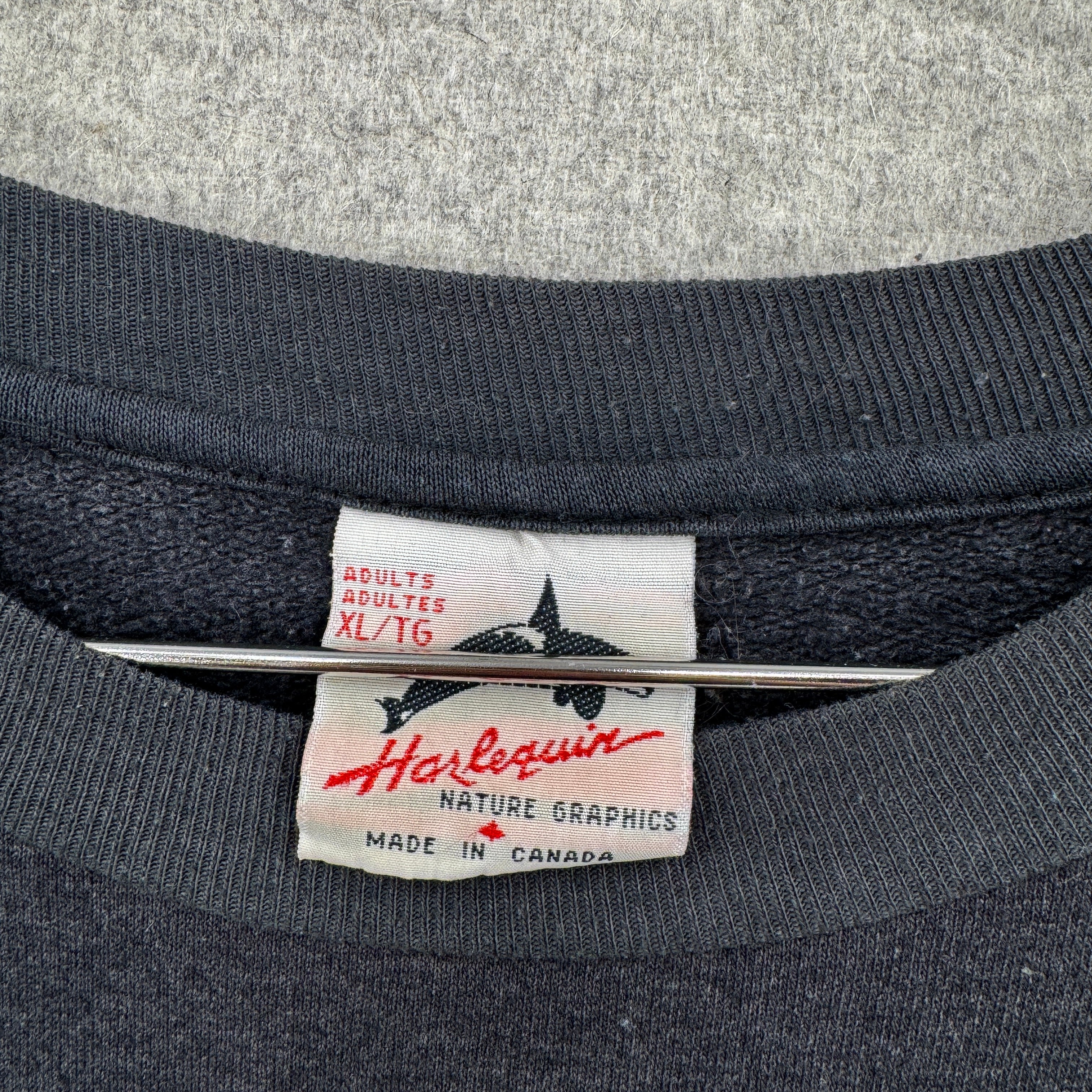 Close-up of a Harlequin label on a dark fabric background. Made in Canada, adult XL size