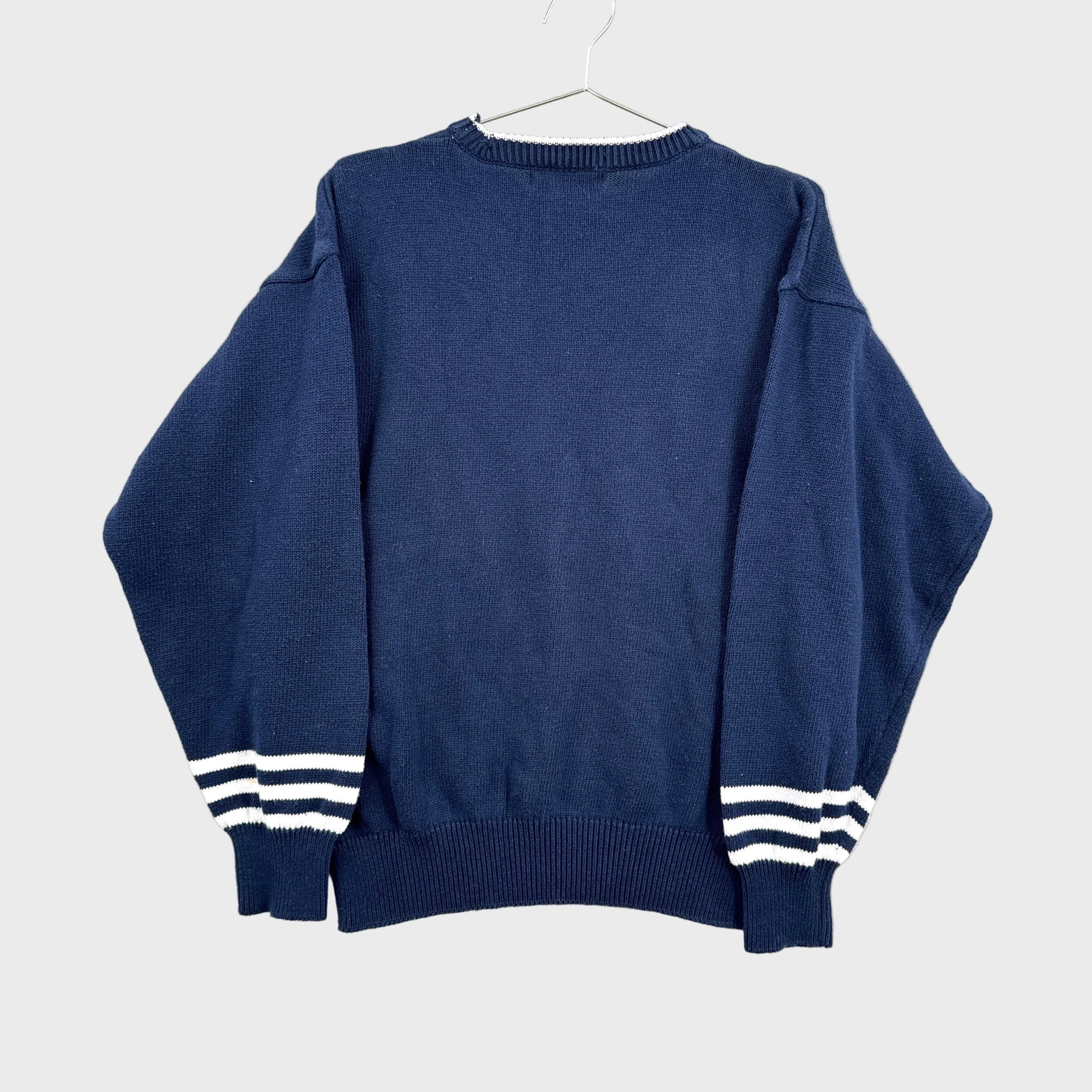 Blue sweater with white stripes on cuffs and hem, hanging on a gray background