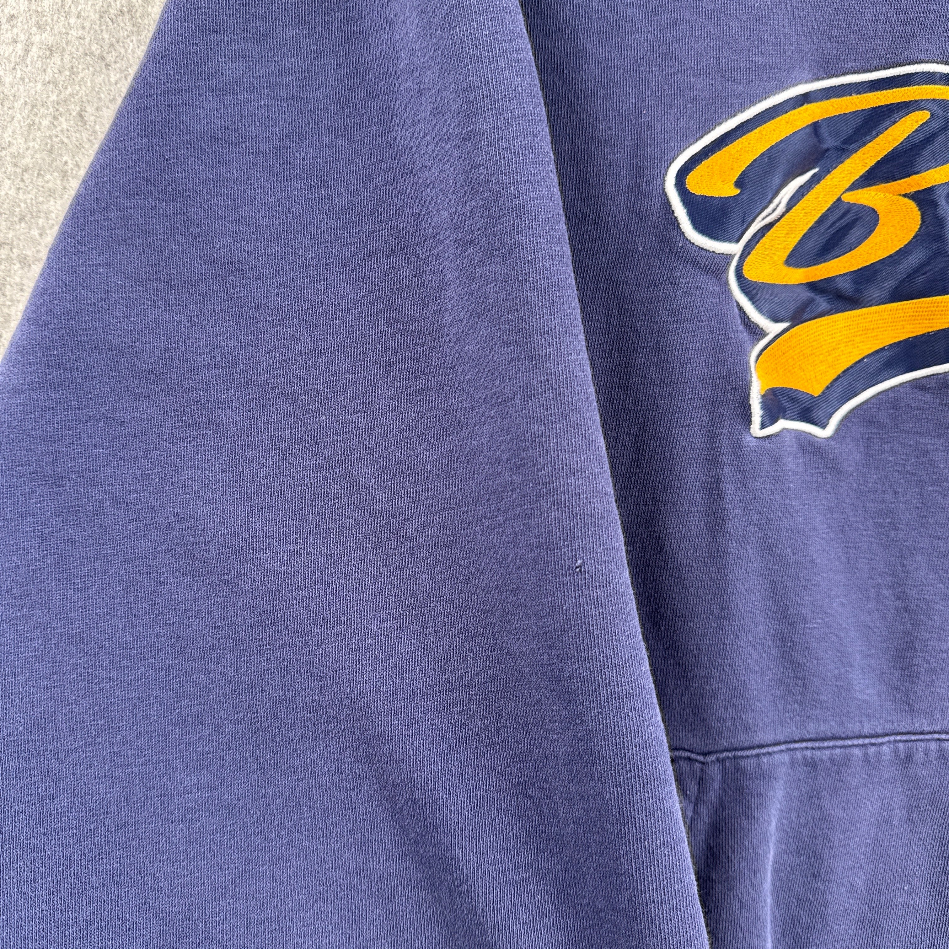 Blue sweatshirt with a yellow and white logo on a textured surface, shows small hole on sleeve
