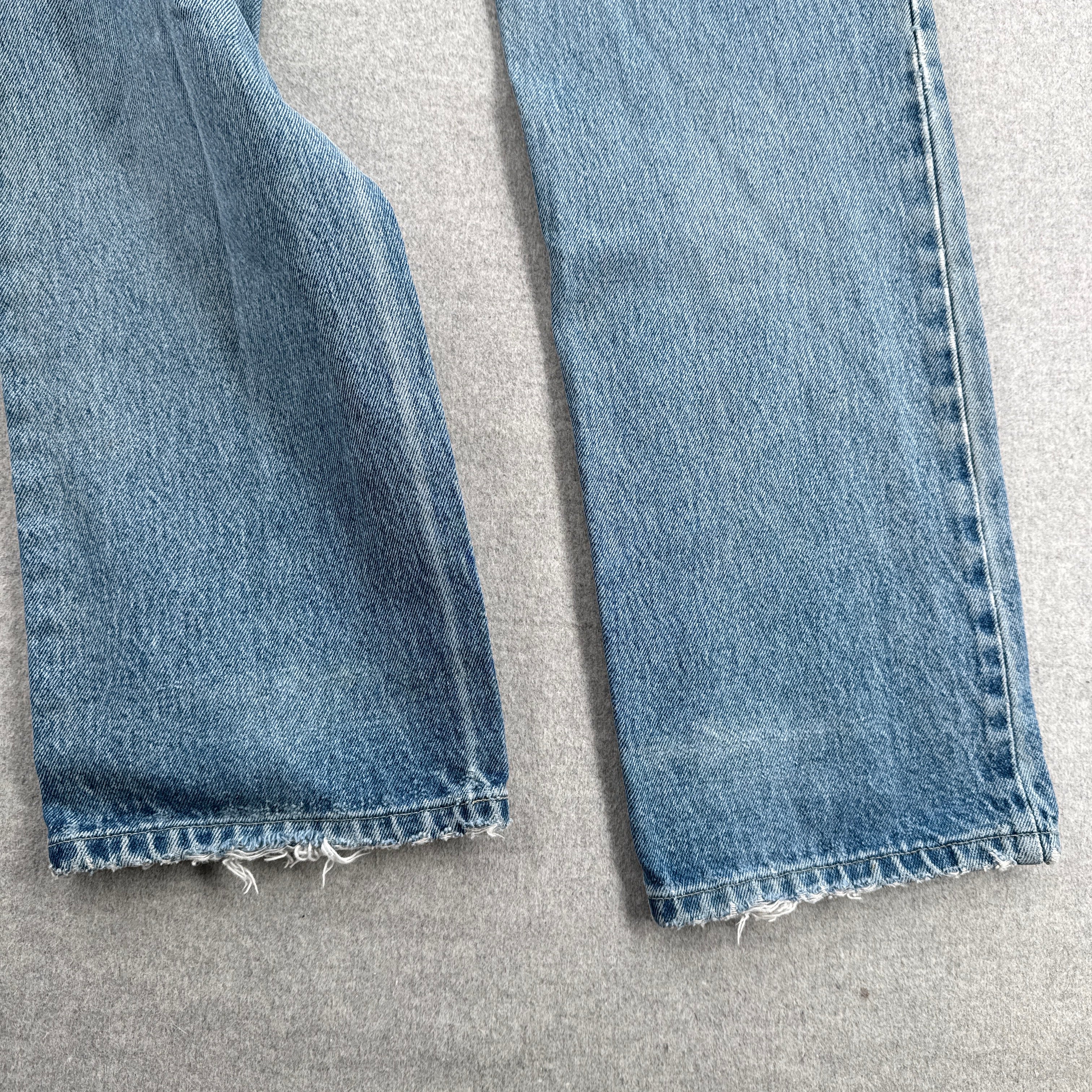 Close-up of blue jeans with frayed hems on a gray surface